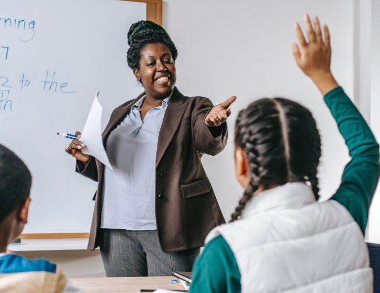 Older African American teacher points to a young Asian student holding her hand up to answer a question. The image represents the importance of ethnic diverse teachers lecturing abroad.